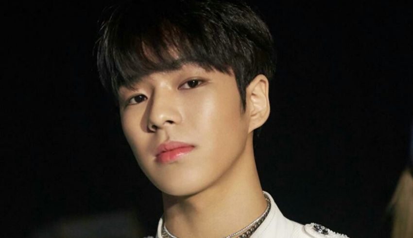 A korean man in a white jacket with a necklace.