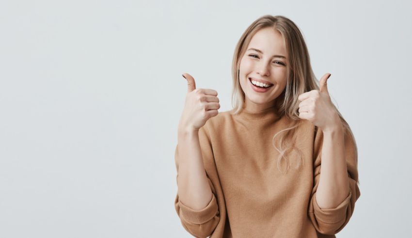 A young woman giving a thumbs up on a gray background.