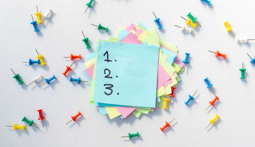 A sticky note with a number of colored pins on it.