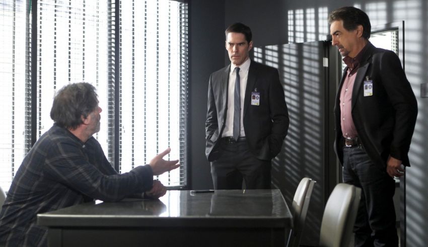 Three men sitting at a desk talking to each other.