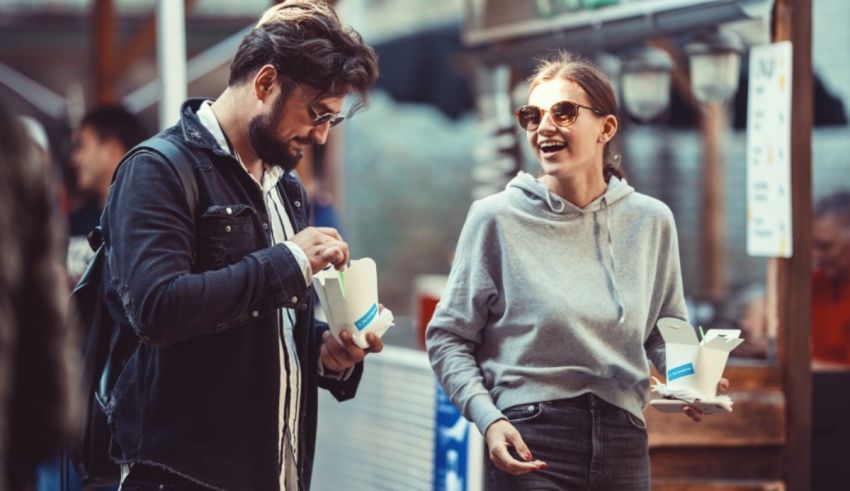 A man and a woman are eating at an outdoor market.