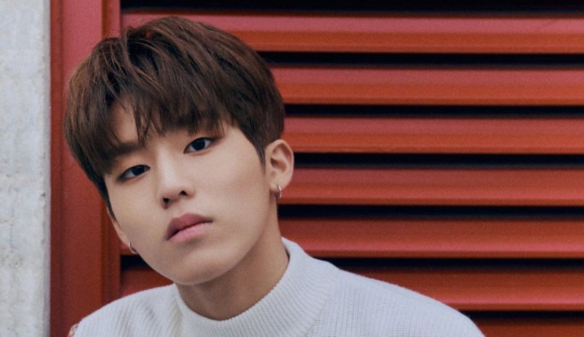 A young man in a white sweater is standing in front of a red shutter.