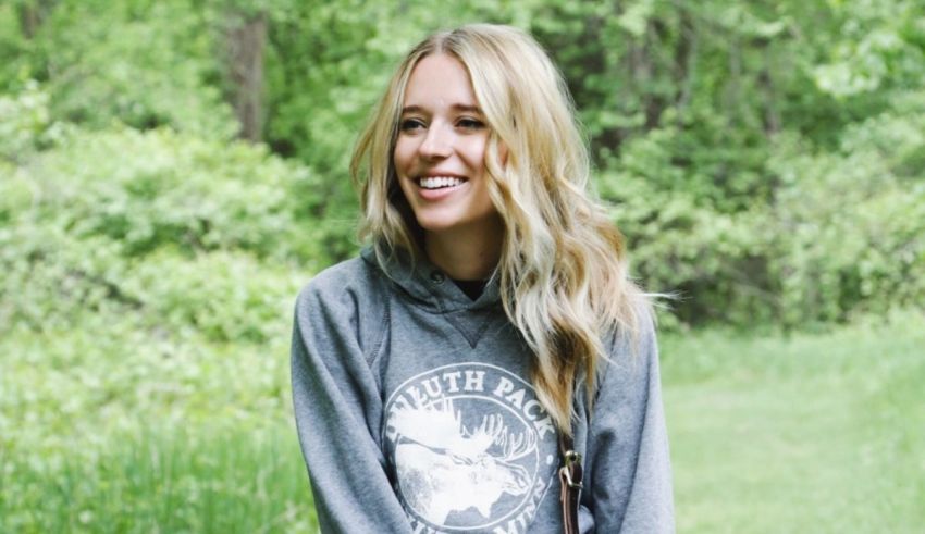 A blonde woman in a gray hoodie sitting in a field.
