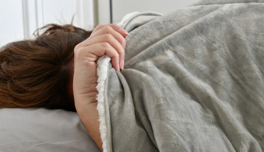 A woman laying in bed with a blanket over her head.