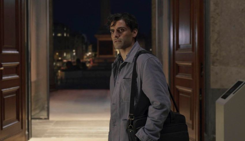 A man in a grey coat standing in front of a door.