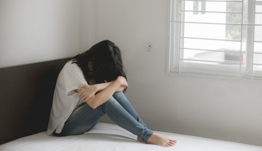 A woman sitting on a bed with her hands on her knees.