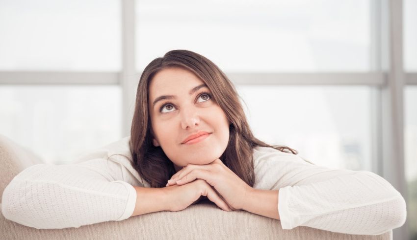 A woman is sitting on a couch looking up at the window.