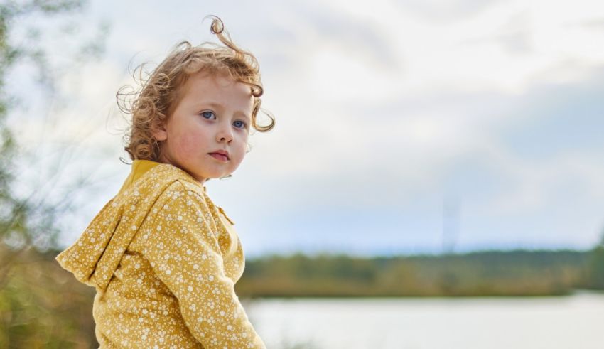 A little girl is standing near a body of water.