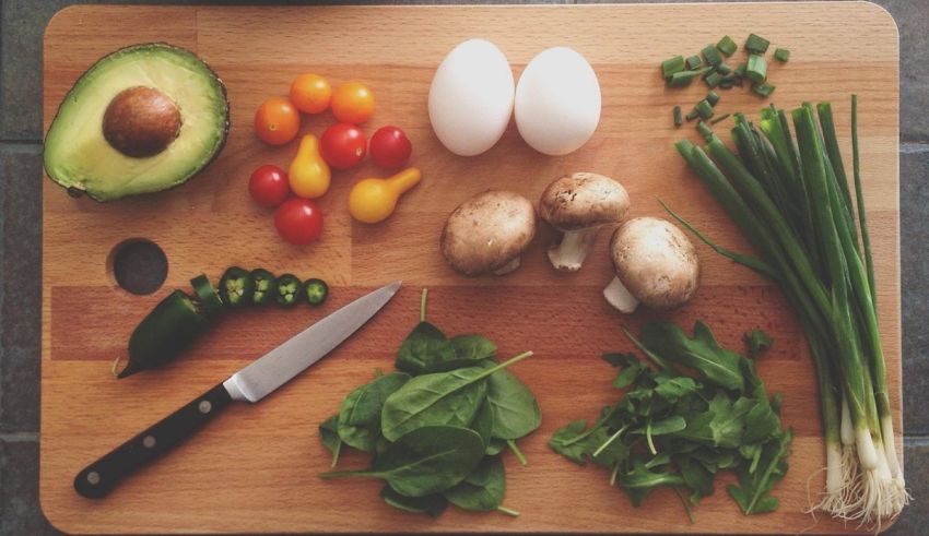 A cutting board with vegetables, eggs, avocado, and a knife.