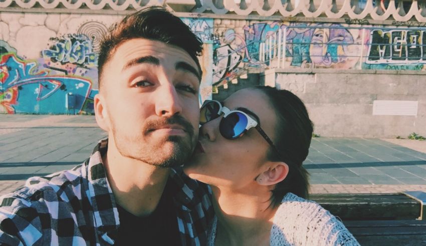 A man and woman taking a selfie in front of a graffiti covered wall.