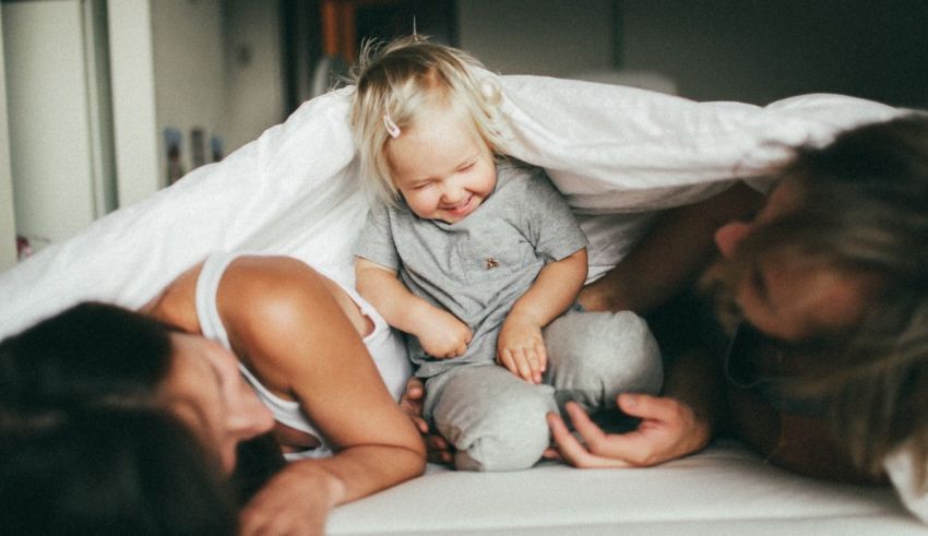 A family laying on a bed with a child under a blanket.