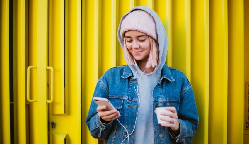 A girl wearing a hoodie is holding a cup of coffee and listening to music.