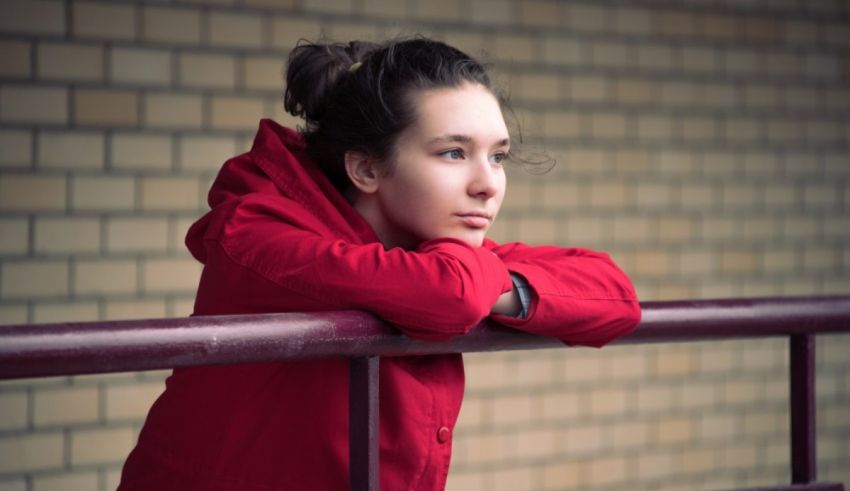 A young woman in a red coat is leaning against a railing.
