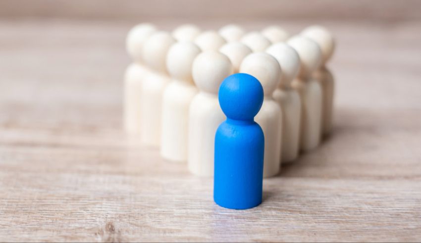 A blue figure standing in the middle of a group of wooden figurines.