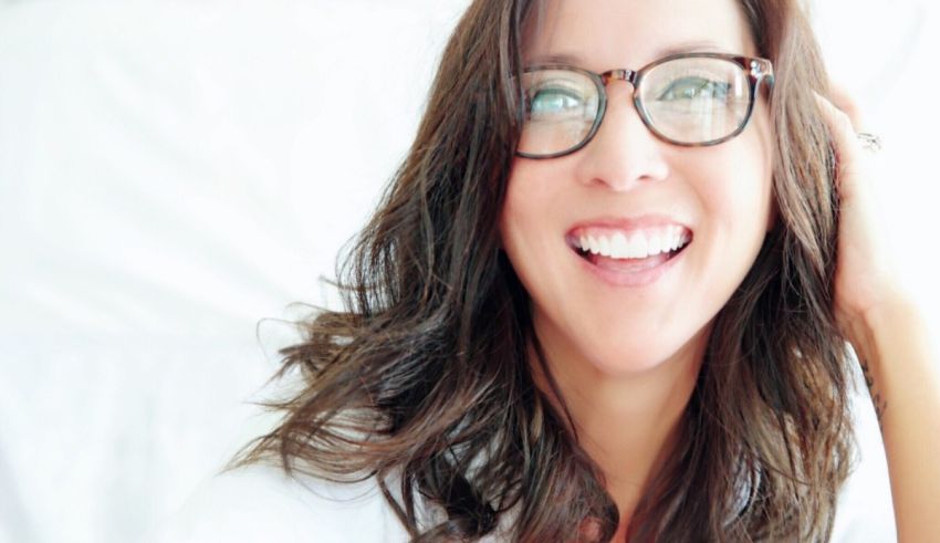 A woman in glasses smiling while laying on a bed.