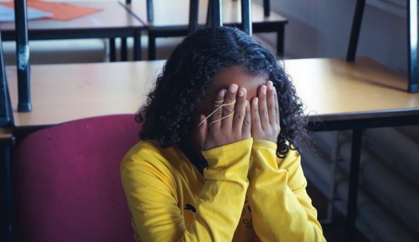 A girl with her hands covering her face in a classroom.
