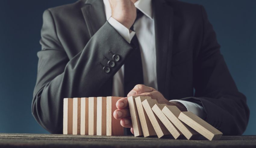A businessman in a suit is holding dominoes on a table.
