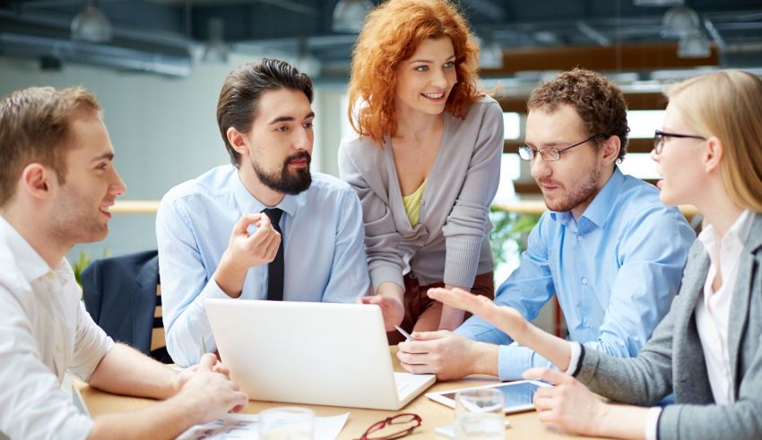 A group of people sitting around a table looking at a laptop.