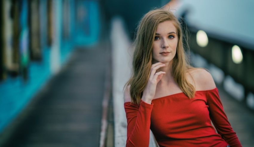 A young woman in a red top leaning against a railing.