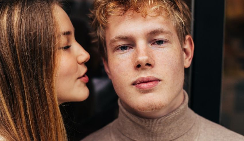 A young man and woman kissing in front of a window.