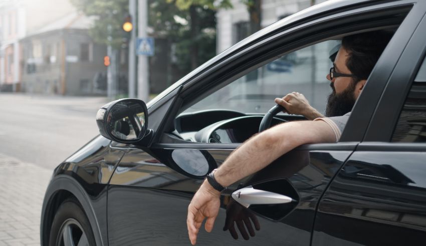 A man is driving a car with his hand out of the window.