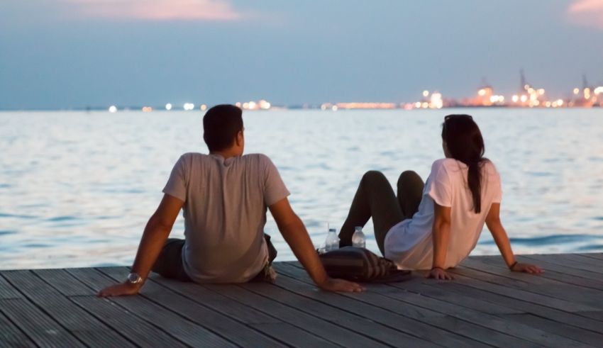 Two people sitting on a dock looking at the water.