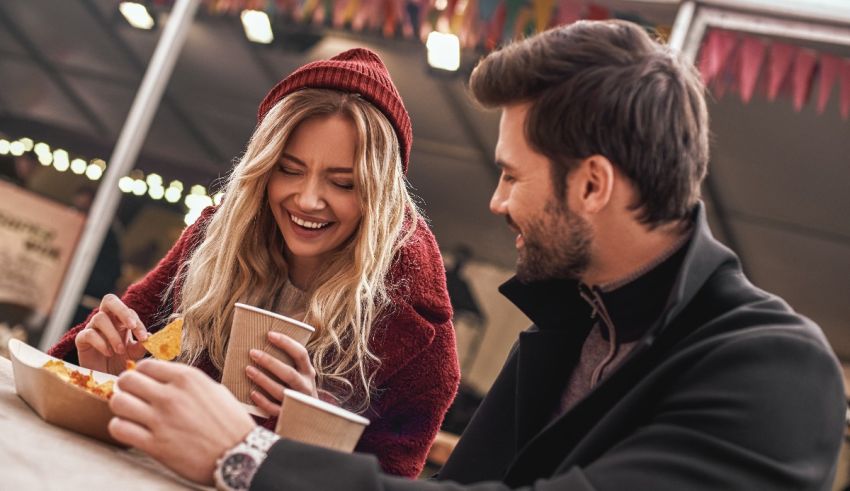 A man and woman eating food at an outdoor market.