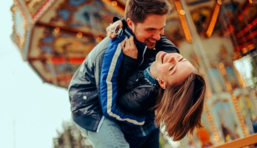 A man and woman hugging in front of a carousel.