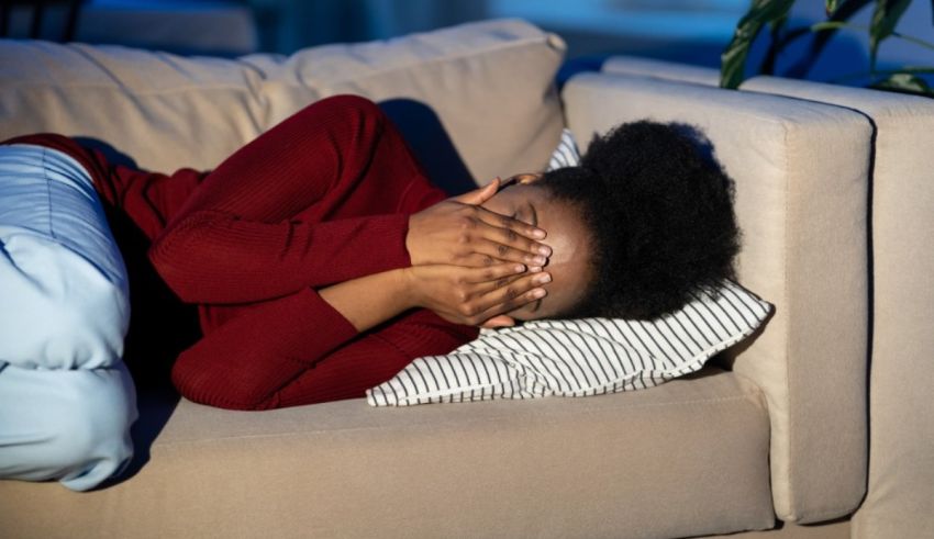 A woman covering her face while sitting on a couch.