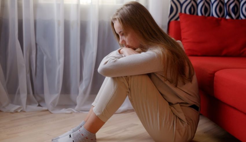 A young woman sitting on the floor in front of a red couch.