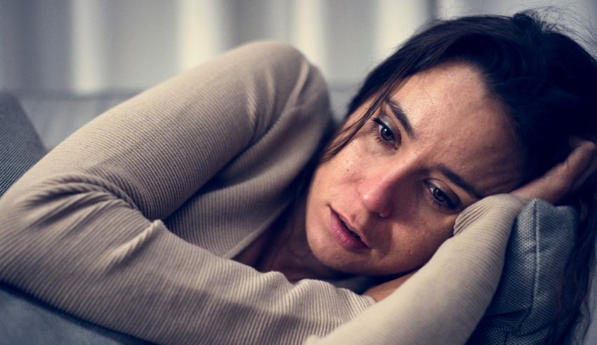 A woman is sitting on a couch with her head resting on her hand.