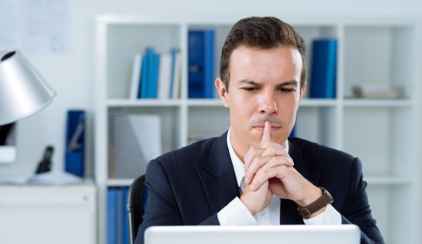 A businessman with his finger on his lips in front of a laptop.