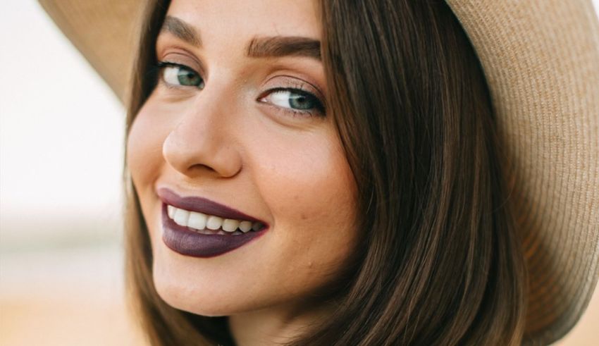 A young woman wearing a straw hat and purple lipstick.