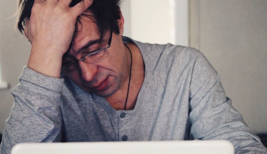 A man holding his head while working on a laptop.