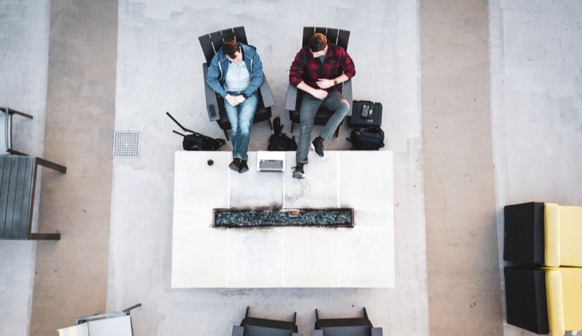Two men sitting on a table in an office.