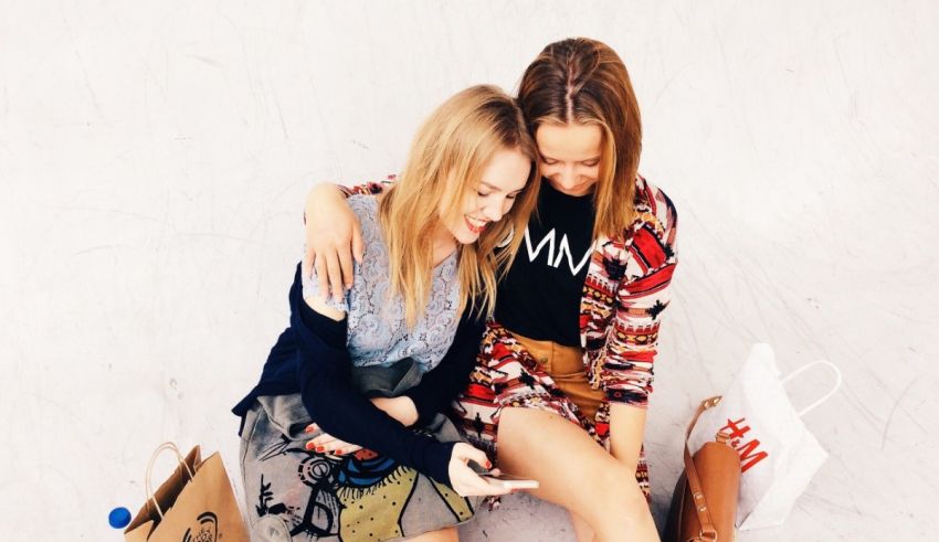 Two women sitting on the floor holding shopping bags.