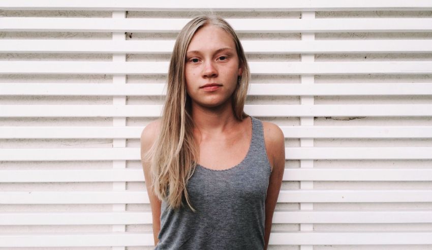 A young woman in a gray tank top standing in front of a white wall.