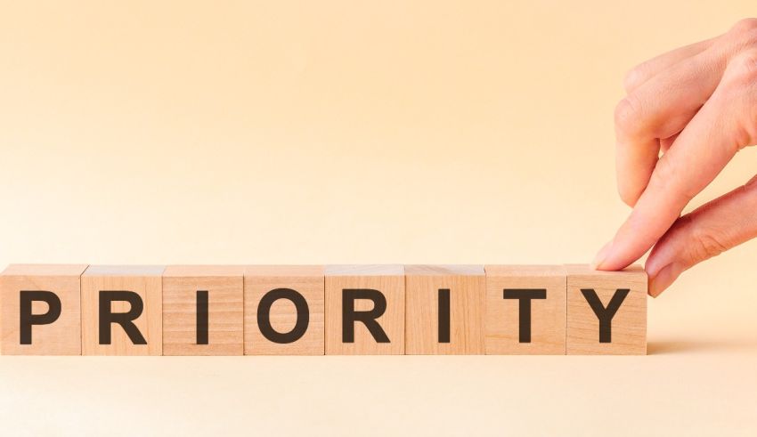 A hand is holding a wooden block with the word priority on it.