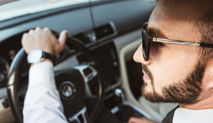 A man driving a car wearing sunglasses and a tie.