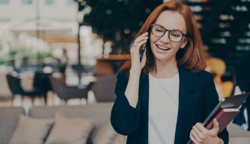 A woman in glasses is talking on the phone while holding a book.