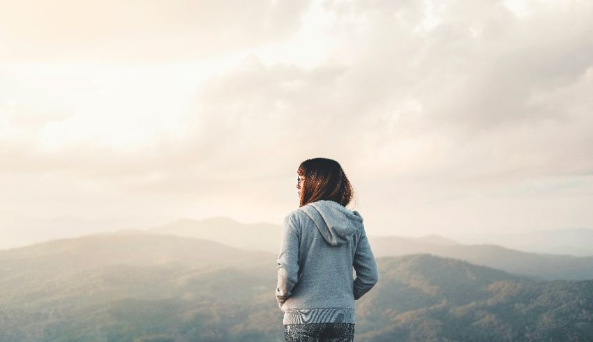 A woman is standing on top of a mountain overlooking a valley.
