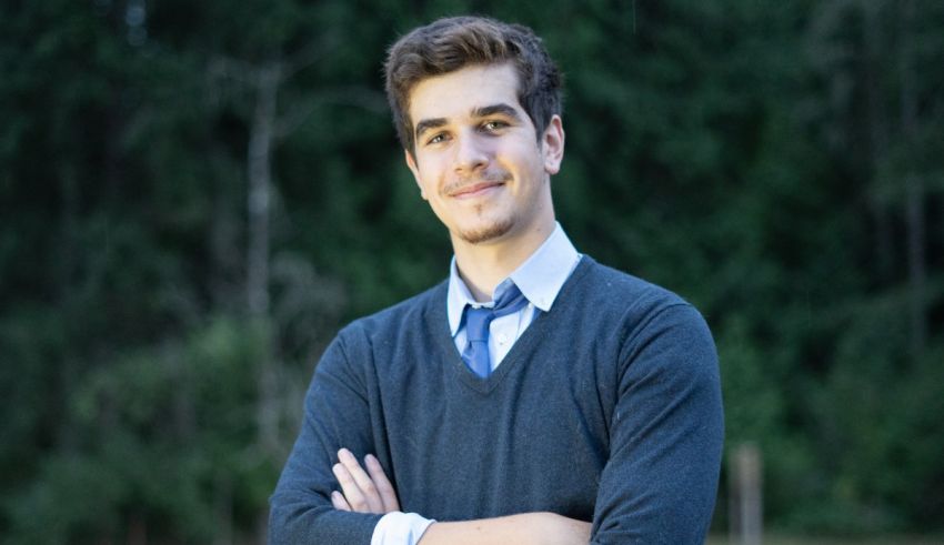 A young man with his arms crossed in front of a forest.