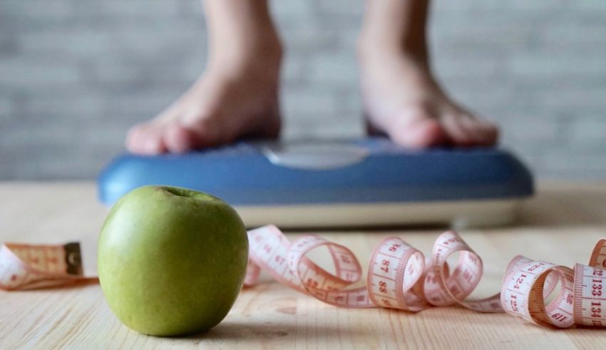 A woman's feet on a scale next to a green apple.
