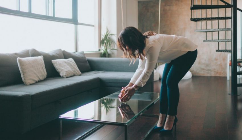 A woman standing on a glass coffee table in a living room.