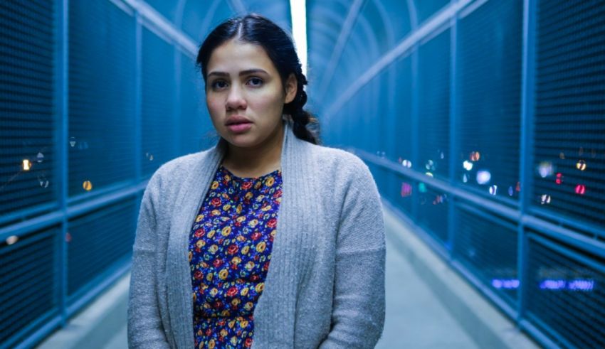 A young woman standing in a blue tunnel at night.