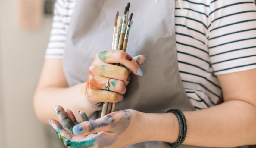 A woman in an apron with paint brushes in her hands.