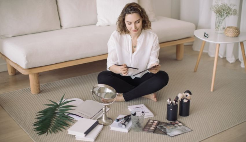A woman sitting on the floor with a notebook and cosmetics.