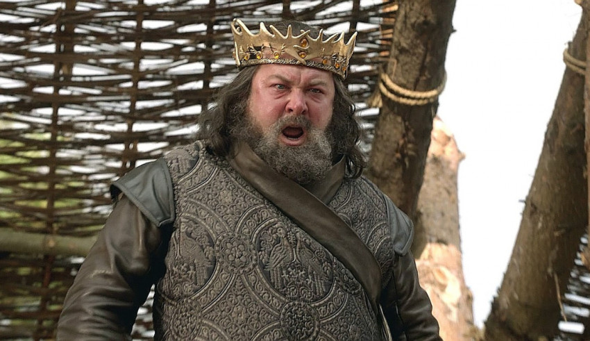 A bearded man with a crown in front of a tree.