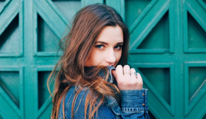 A woman in a denim jacket leaning against a green door.