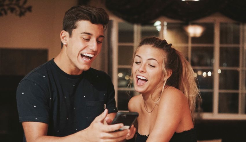 A man and woman laughing while looking at a cell phone.